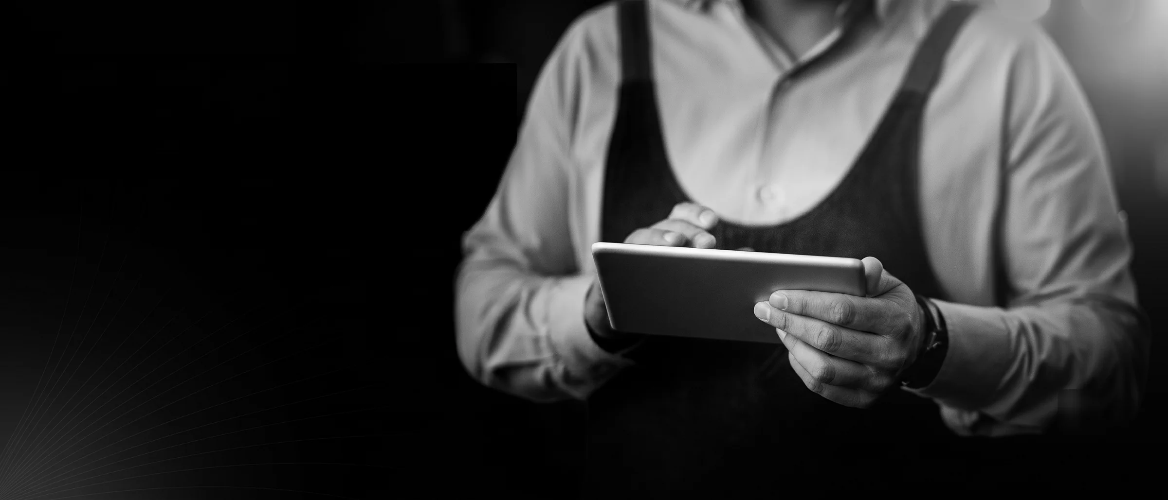 Anfitrión de restaurante consultando una tablet en un comedor a oscuras; la pantalla es la única fuente de luz.